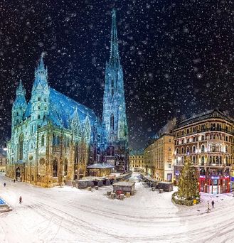 Der Stephansdom wird grün-blau angeleuchtet und erstrahl im dunklen Nachthimmel. DIe Straße ist von einer Schneedecke bedeckt und in der Luft schirren dicke Schneeflocken.