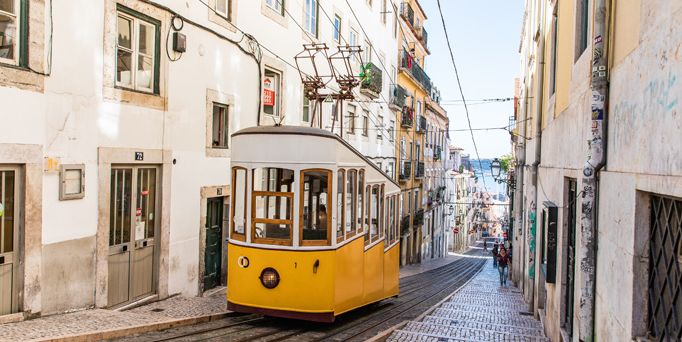 In einer engen, steilen Gasse mit weiß-beigen Häusern befindet sich eine gelbe Straßenbahn.