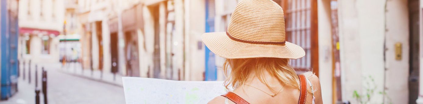 Valentinstag 2026: Eine frau mit Sonnenhut läuft mir einem Stadtplan durch eine mediterrane Gasse