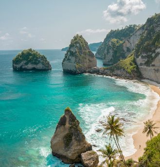 Strandurlaub Asien: Ein menschenleerer Strand mit tropischen Palmen zwischen Felsen