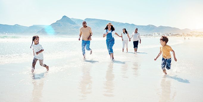 Eine Familie rennt an einem belebten Strand durch das seichte Wasser