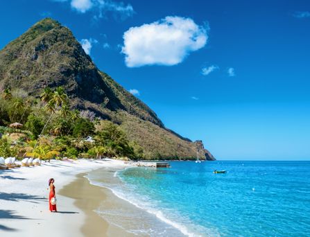 Reiseziele weltweit: Eine Frau steht an einem weißen Sandstrand, hinter ihr tropische Vegetation