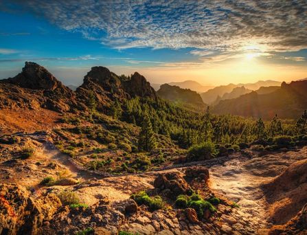 Eine bergige, teils begrünte Landschaft unter dem Sonnenuntergang